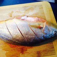 大黄鱼像这样两边斜切几刀，在鱼身上均匀的摸上料酒，再摸上盐腌制15分钟。