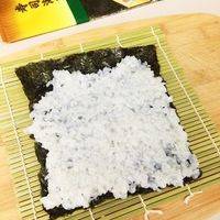 把寿司海苔放在竹席上，接着将米饭铺在海苔上压实（注意：海苔留2厘米不要铺米饭）