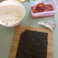 准备好所有食材，将紫菜片铺在寿司帘上。将寿司醋滴进米饭中，搅拌。