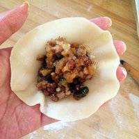 我是现买的饺子皮 用擀面杖把边缘擀薄 手中握馅儿 在收口处挤一下 然后用勺子把虎口抹平